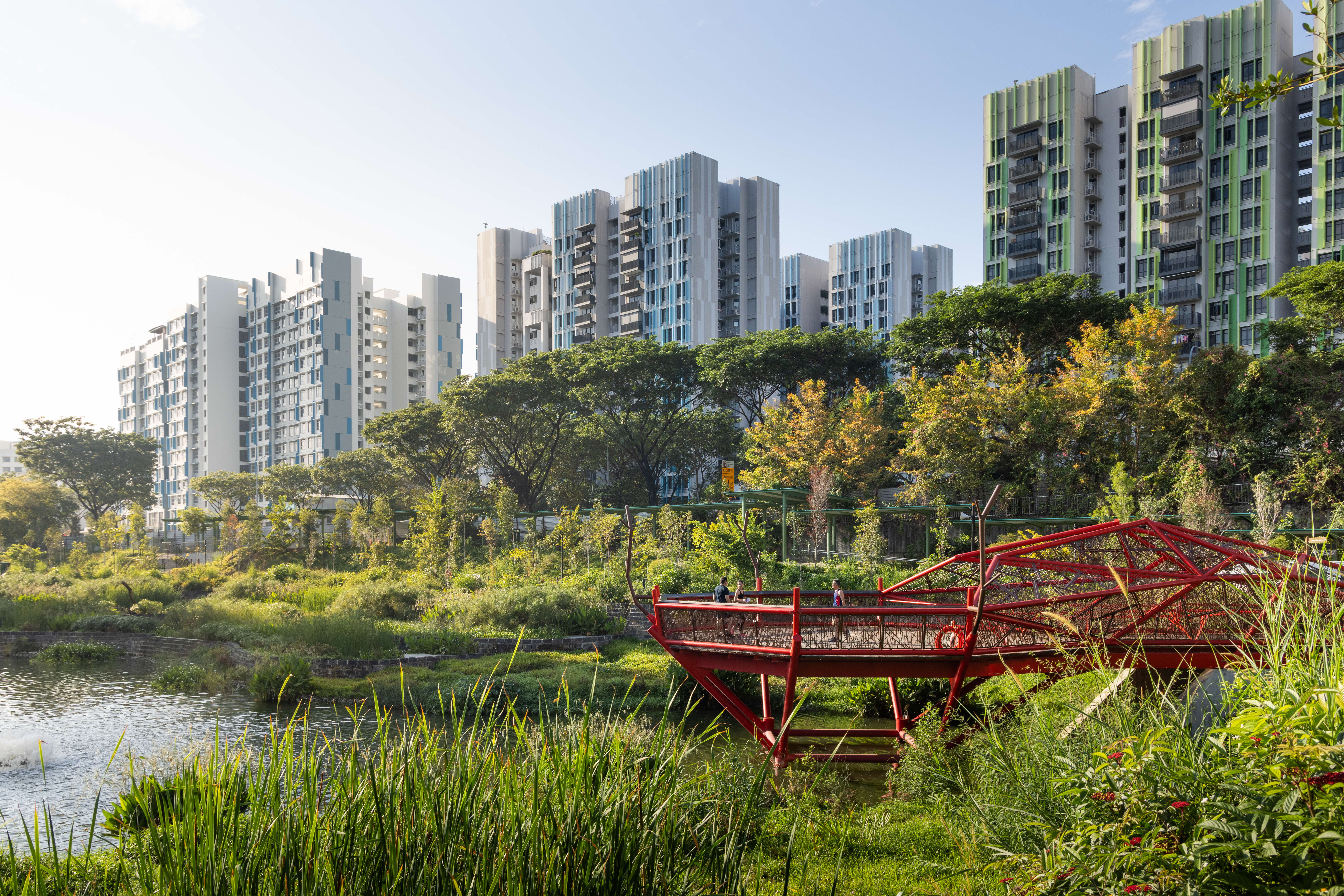 Red bridge and lakeside greenery with residential buildings in the background.